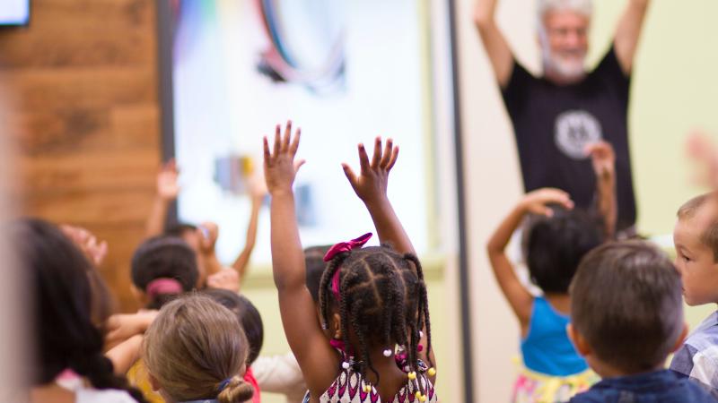 Young children raising their hands in class.