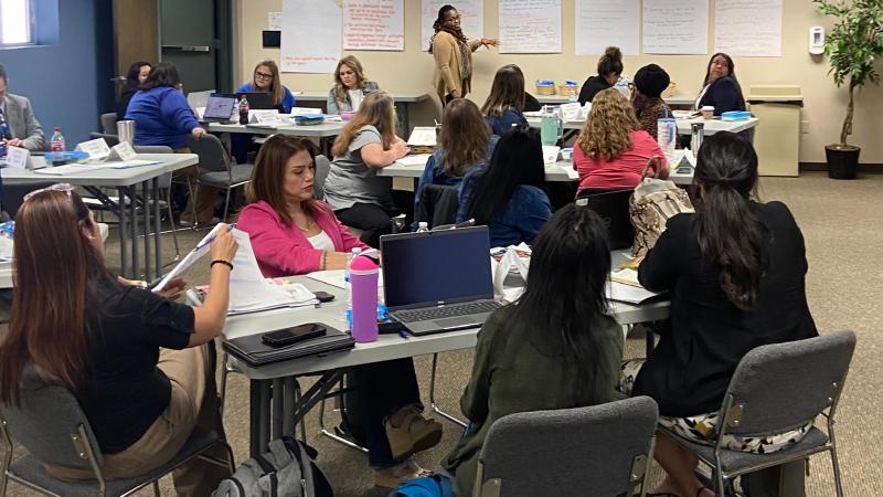 Group of educators sitting at tables listening to colleagues share project plans..