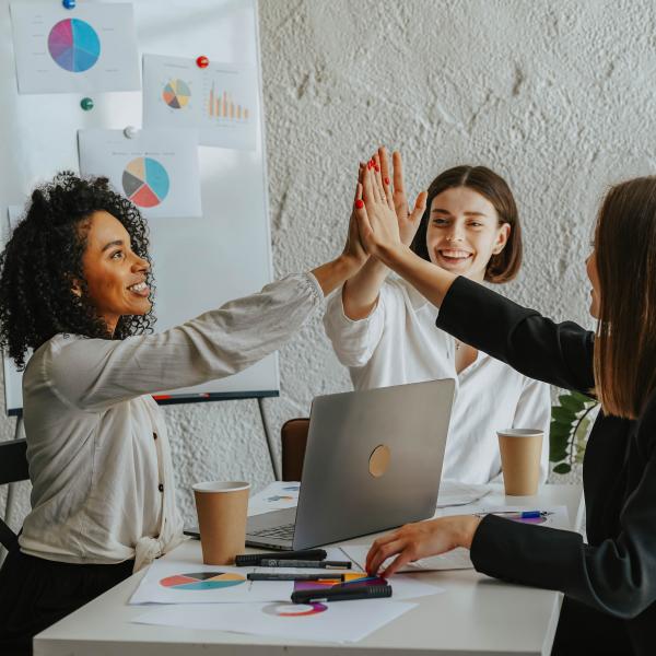 Three women around a table high fiving.